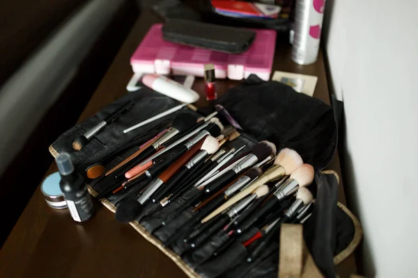 A set of makeup brushes in an open black cosmetic bag on a wooden table with cosmetics. Makeup artist set.