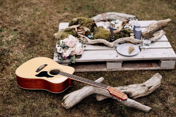 Gitar akustik di rumput dengan latar belakang tribun kayu dengan barang-barang untuk dekorasi. — Stok Foto