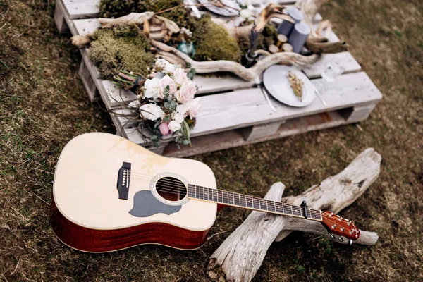 Akustik gitar pada rumput dan bunga, cabang pohon dan lilin di berdiri kayu. — Stok Foto