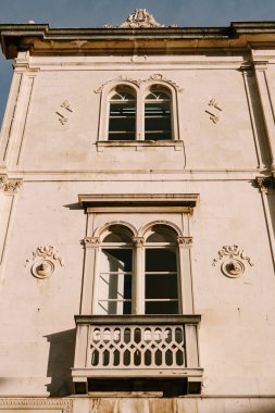 Oval kemerli pencereye yakın çekim. Binanın balkonunda desenler ve taştan bir insan figürü var..