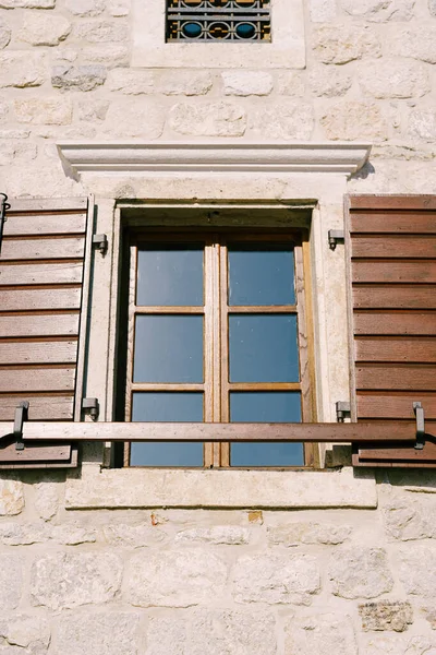 Primo piano di una finestra marrone con persiane in legno e una tavola sulla parete di una casa in pietra. — Foto Stock