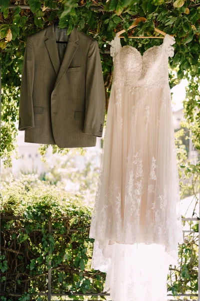 El vestido de novia y los novios chaqueta gris en el arco con hojas verdes en el patio. —  Fotos de Stock