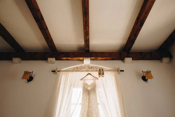 Світла кімната з весільною сукнею на вішалці на карнизі та взутті наречених . — стокове фото