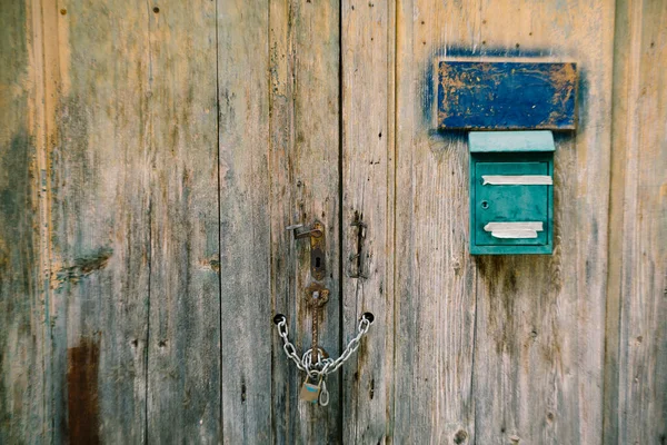 An old green mailbox on a dilapidated wooden gate with a chain wrapped handle and a padlock. — Stock Photo, Image