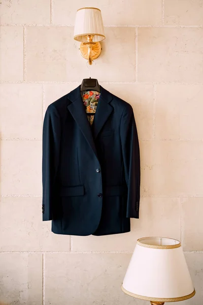 Una chaqueta azul con forro colorido en una percha negra cuelga de una lámpara de pared en una habitación con una lámpara de mesa. —  Fotos de Stock