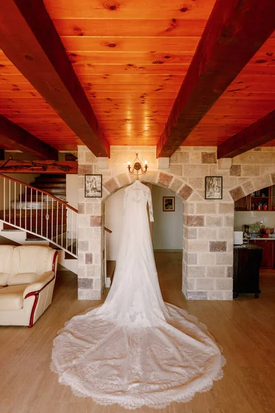 Біла сукня нареченої з довгим поїздом у кімнаті з кам'яною аркою, білим диваном і сходами на другий поверх . — стокове фото