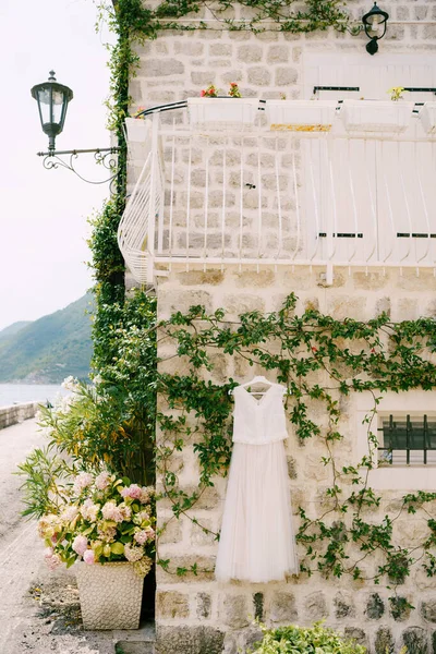 Весільне вбрання нареченої на тлі кам'яної стіни будинку з балконом на другому поверсі і жасмин звивається вздовж стіни, в старій віллі в Пересті, Чорногорія.. — стокове фото