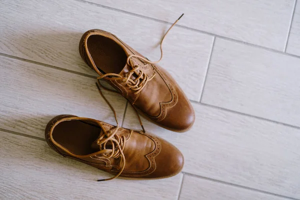 Brown mens shoes with untied laces on a white laminate.