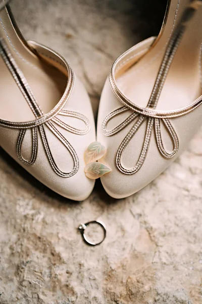 Pendientes para mujer en forma de hojas en los dedos de los pies de las novias zapatos blancos con un anillo de compromiso en una textura áspera. —  Fotos de Stock