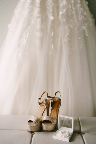 Las novias zapatos de boda de oro, pendientes y una pulsera de perlas en el fondo del vestido de novia. —  Fotos de Stock