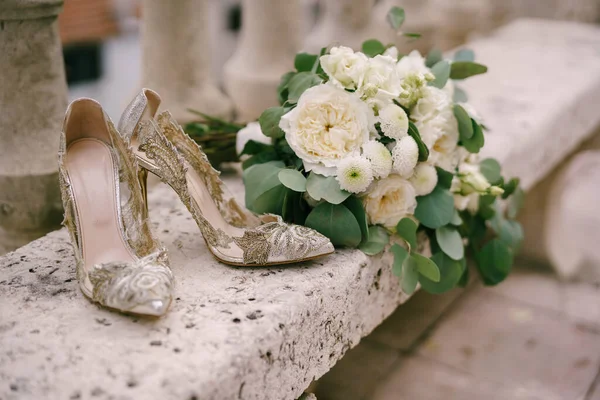 Elegantes zapatos de mujer con patrones en tacones altos en un banco con un ramo de flores blancas. —  Fotos de Stock