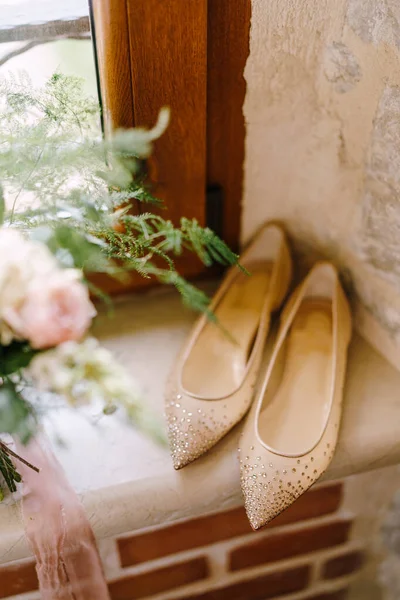 Un alféizar junto a una ventana de madera con un ramo de flores y zapatos de ballet con pequeñas piedras brillantes. —  Fotos de Stock