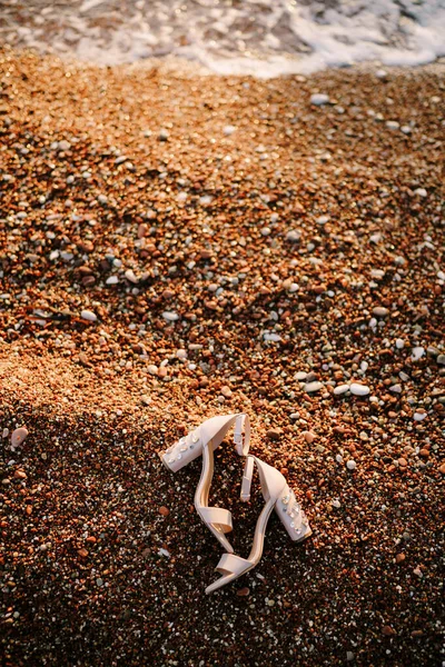 Bruids sandalen met dikke hakken versierd met stenen op een kiezelstrand aan zee. — Stockfoto
