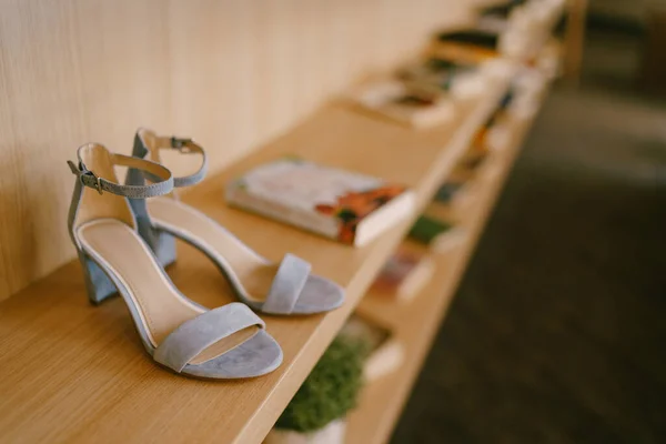 Sandalias de tacón gris en un estante de madera con libros en poca profundidad de campo. —  Fotos de Stock