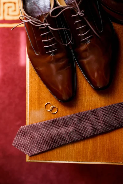 Homens sapatos de couro marrom com um laço e anéis de casamento em uma mesa de madeira na sala. — Fotografia de Stock