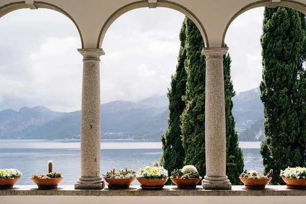 Blomkrukor med saft i valv med pelare med utsikt över sjön Como i Italien. — Stockfoto