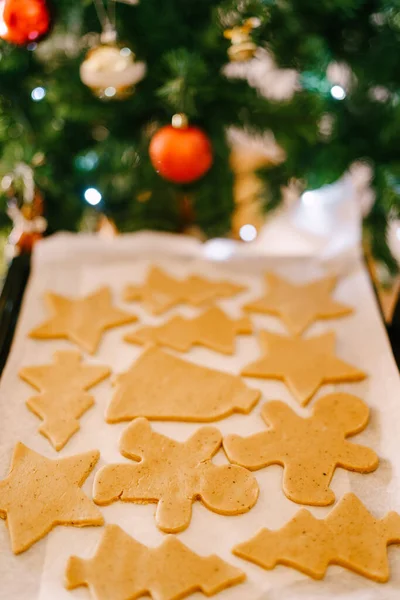 Close-up of uncooked gingerbread dough on white. tray, against the background of a decorated Christmas tree with balls and garlands.