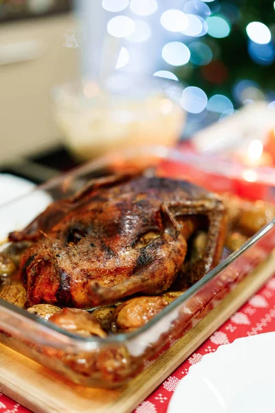 クリスマスツリーのガーランドのライトを背景に、お祝いのテーブルの上にクリスマスダックのクローズアップ。鶏はジャガイモとリンゴを自分の脂肪でカリカリになるまで焼きます. — ストック写真