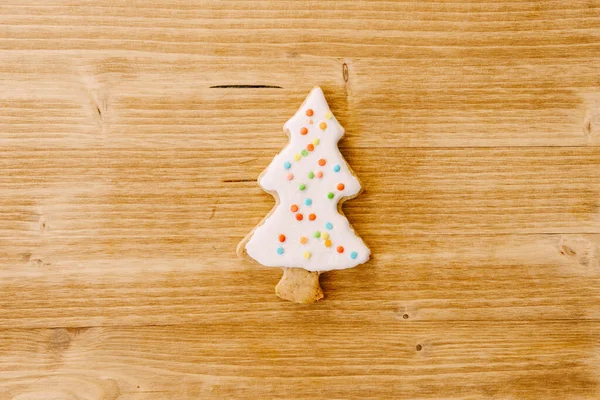 Bellissimi biscotti di pan di zenzero a forma di albero di Natale, decorati con smalto bianco con punti multicolori, contro una superficie di legno leggera. — Foto Stock