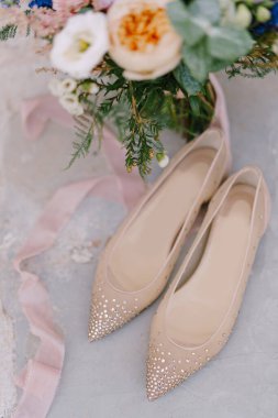 Gelin balesinin yakın çekimleri, parlak taşlar, bir buket çiçek ve beyaz arka planda ipek bir kurdele..