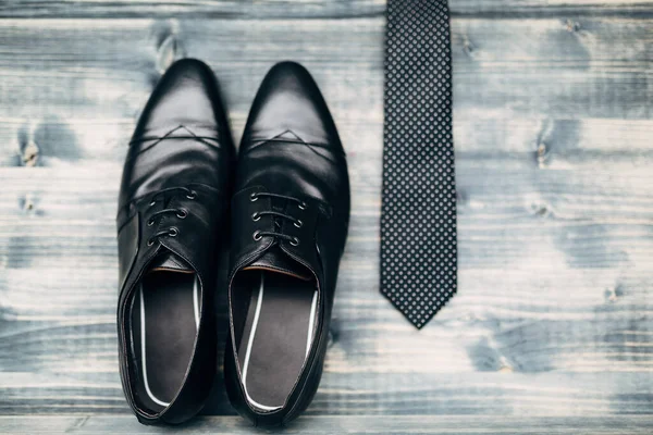 Zwarte leren herenschoenen met een zwarte stropdas met witte stippen op een grijze houten textuur. — Stockfoto