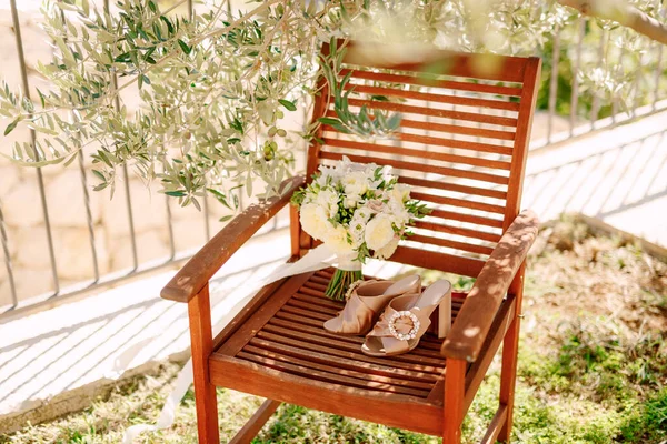 Zuecos beige con una hebilla redonda en una silla de madera con un ramo de flores blancas de la novia atado con una cinta. —  Fotos de Stock