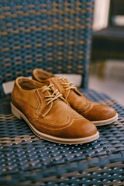 Brown groom shoes on a chair seat in a room with shallow depth of field.