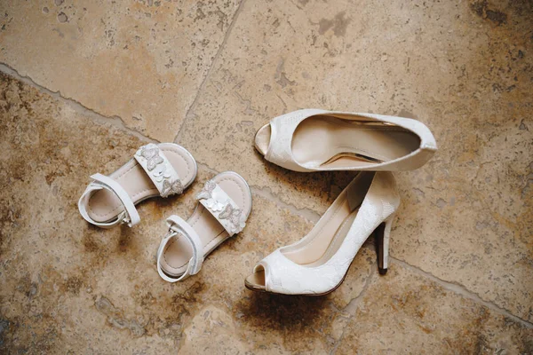 Kvinnors vita öppna tå skor och små flickor vita sandaler på marmor golvet. — Stockfoto