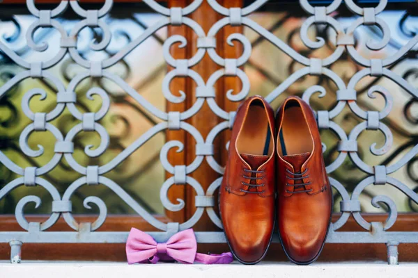 Nowe brązowe męskie buty i muszka z niewiązaną wstążką na oknie w metalowej kratce na zewnątrz. — Zdjęcie stockowe