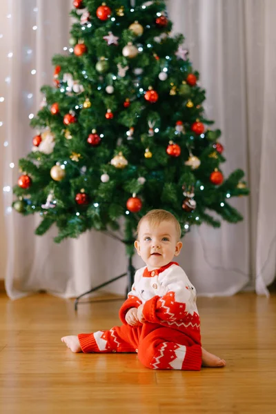 Baby in a knitted red and white onesie in front of a Christmas tree Stock Photo