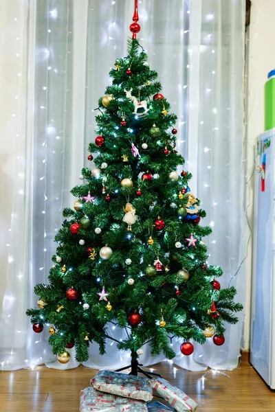 Uma bela árvore de Natal verde com brinquedos embalados embaixo, contra o fundo de guirlandas no interior do apartamento. — Fotografia de Stock