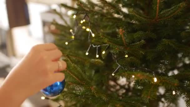 Les mains des femmes décorent le sapin de Noël avec une boule bleue. — Video