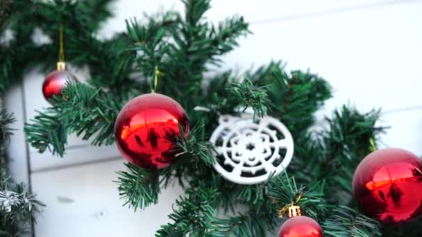 하얀 나무 배경에 있는 크리스마스 장식 - 붉은 공이 달린 전나무 가지와 커다란 붉은 활. — 비디오