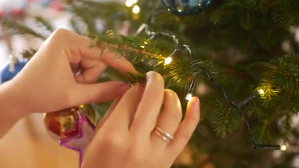 Mãos femininas pendurar uma bola dourada com brilhos no ramo de uma árvore de Natal. — Vídeo de Stock