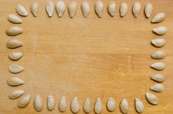 pumpkin seeds lined up, with the tip of the seed pointing to the center of the photo on a wooden surface