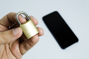 Cep telefonlarında güvenliğin kavramsal fotoğrafı. Arka planda kapalı bir asma kilit ve bir cep telefonu tutan el.