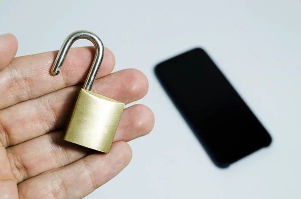 Photo conceptuelle de la sécurité sur les téléphones mobiles. Main tenant un cadenas ouvert et un téléphone portable en arrière-plan — Photo