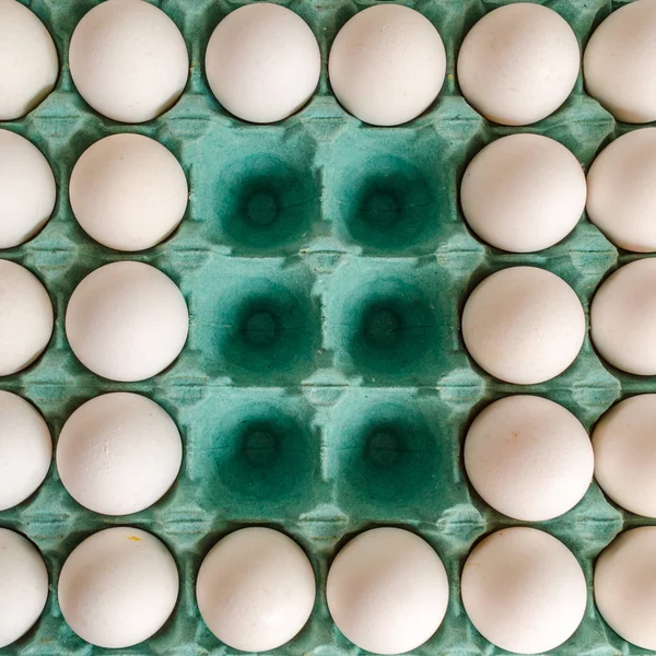 White eggs arranged together in a green egg carton with empty spaces in the middle.