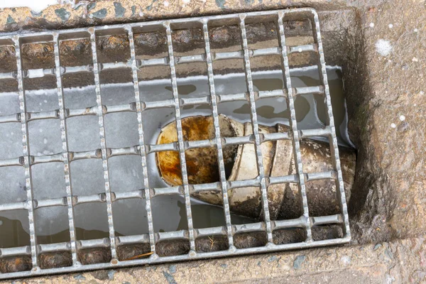 A white water pipe in a drain where water is collected and channeled down the drain