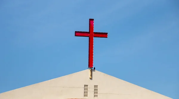 A Close up view of a red cross on top of a church roof on a sunny summers day