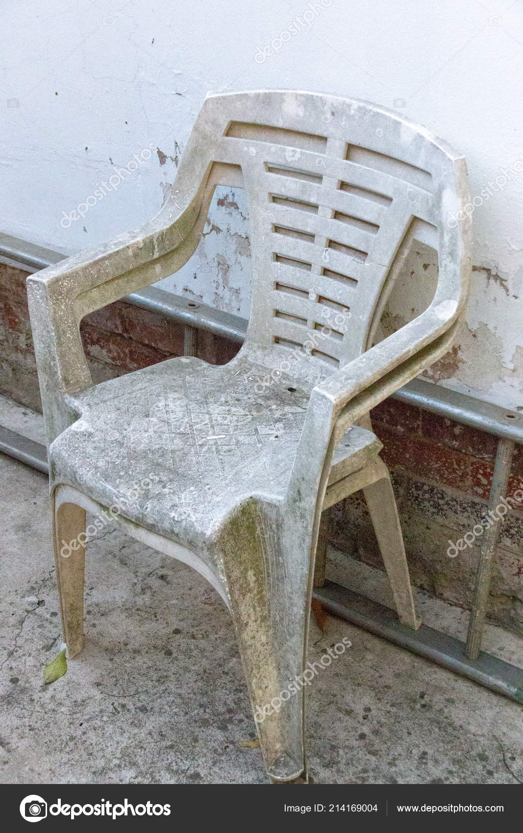 a close up view of two very old white plastic chairs up against the side of  a metal ladder and white wall 214169004