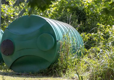 Kapsayıcı veya yüklenmek üzere bekleyen bir bina dışında kendi tarafında yalan tank tutan bir yeşil yağmur su görünümü kadar yakın 