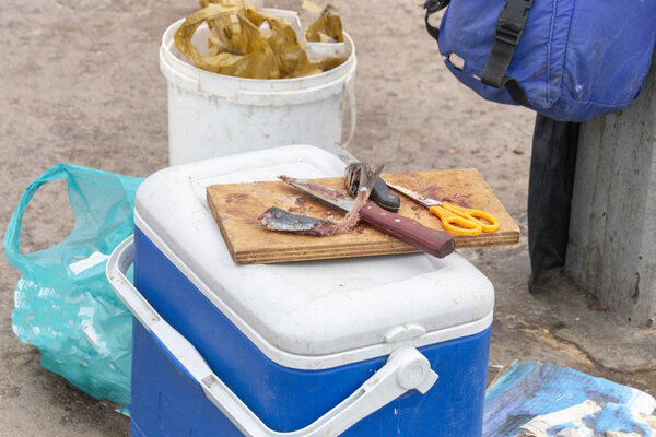 Вид крупным планом на рыбацкую наживку из сардин на деревянной доске с двумя ножами, ножницами из жёлтой ручки, которые были порезаны и использованы для ловли рыбы
 