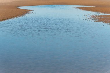 Küçük bir su birikintisi ile alçak sulardan kumdaki dalgaların yakın görüntüsü. 