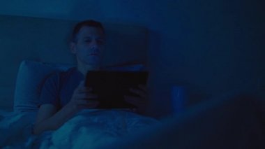 Gece boyunca yatakta bir tablet ile adam