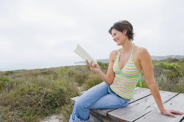 Lächelnde Frau Sitzt Auf Der Strandpromenade Der Natur Und Liest — Stockfoto