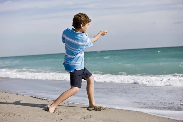 ビーチで海に石を投げる少年 — ストック写真