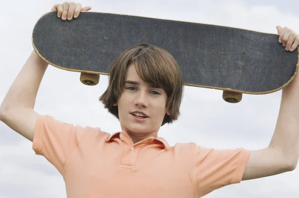 Retrato Adolescente Sosteniendo Monopatín Sobre Cabeza —  Fotos de Stock