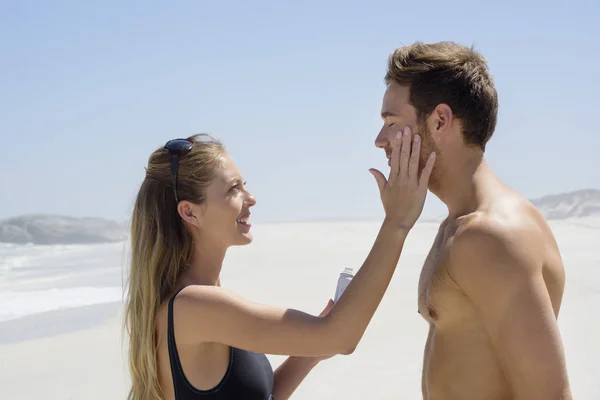 妇女在丈夫面孔应用防晒霜在海滩 — 图库照片