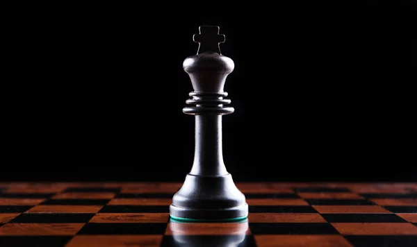 chess piece of a black king on a chessboard on a black background close up